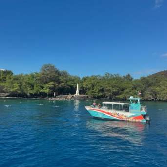 Colorful boat in blue water near a green shoreline with a white monument.
